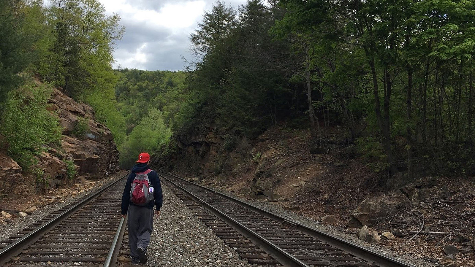 Jasper DiSanto walking along railroad tracks through a wooded landscape