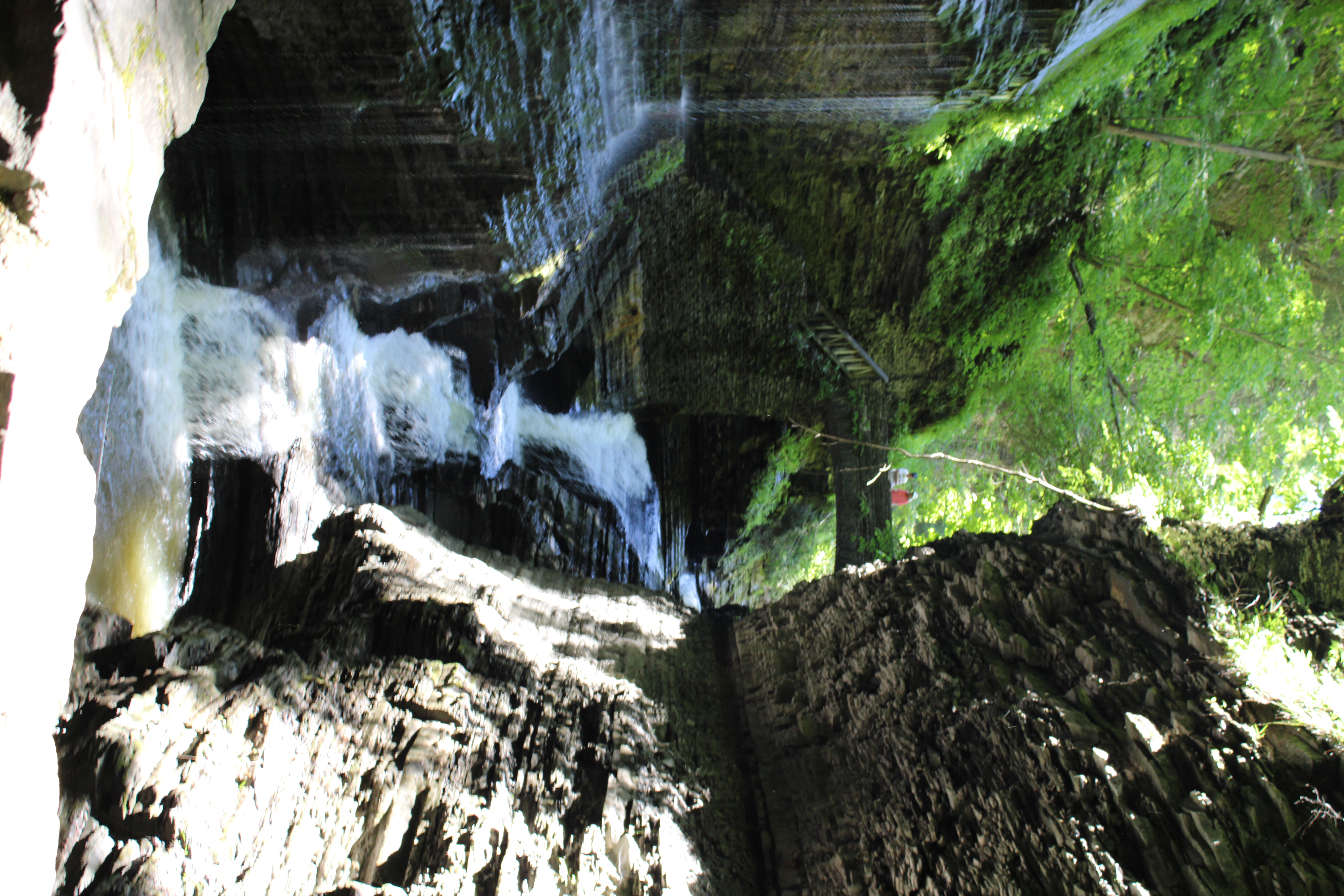 Watkins Glen waterfall framed between dark gorge walls with two visitors on a stone bridge